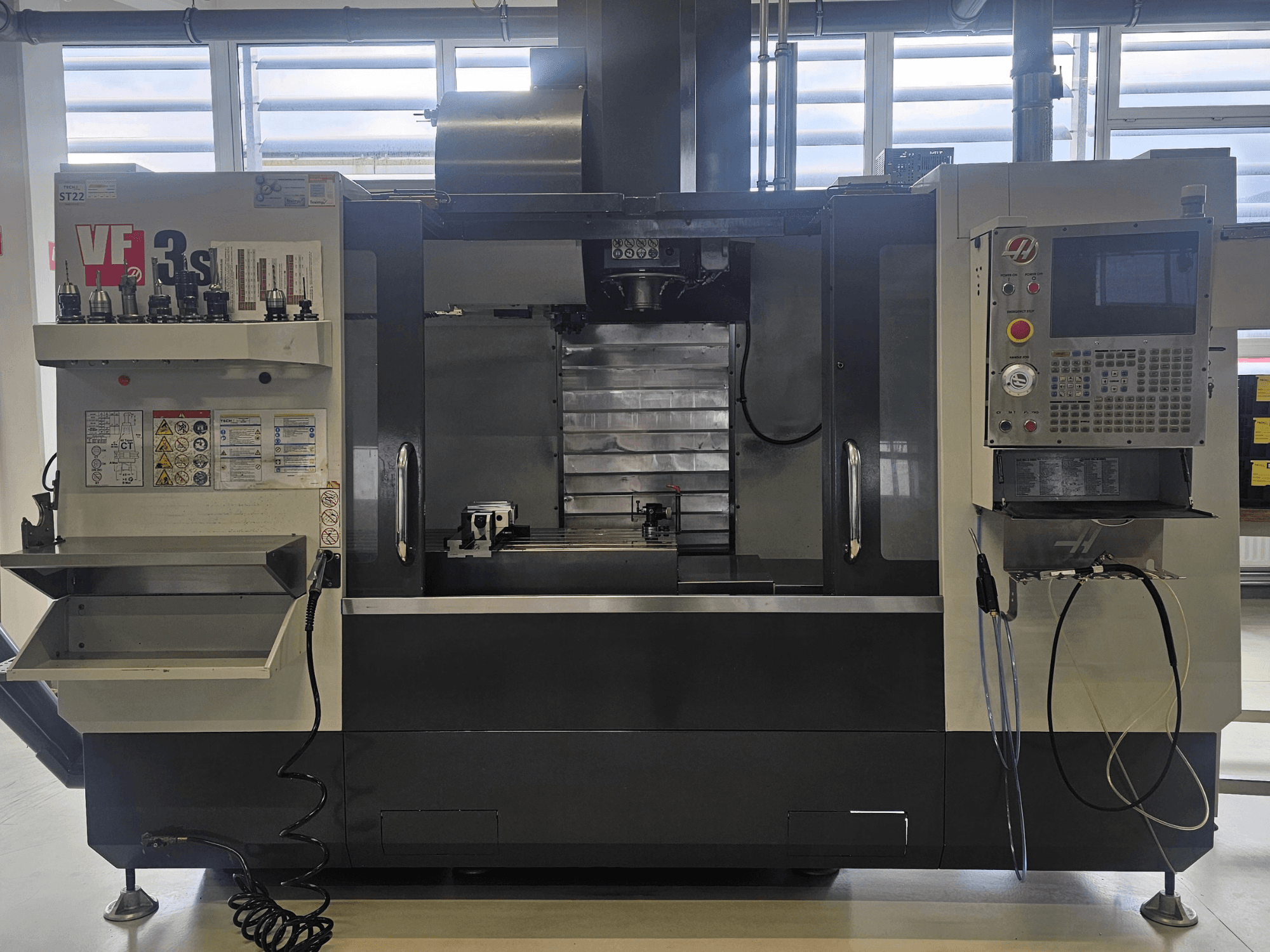 Fresadora CNC Haas VF3SS, vista frontal, con portaherramientas, panel de control y bandeja de refrigerante vacía, con las etiquetas de seguridad visibles.