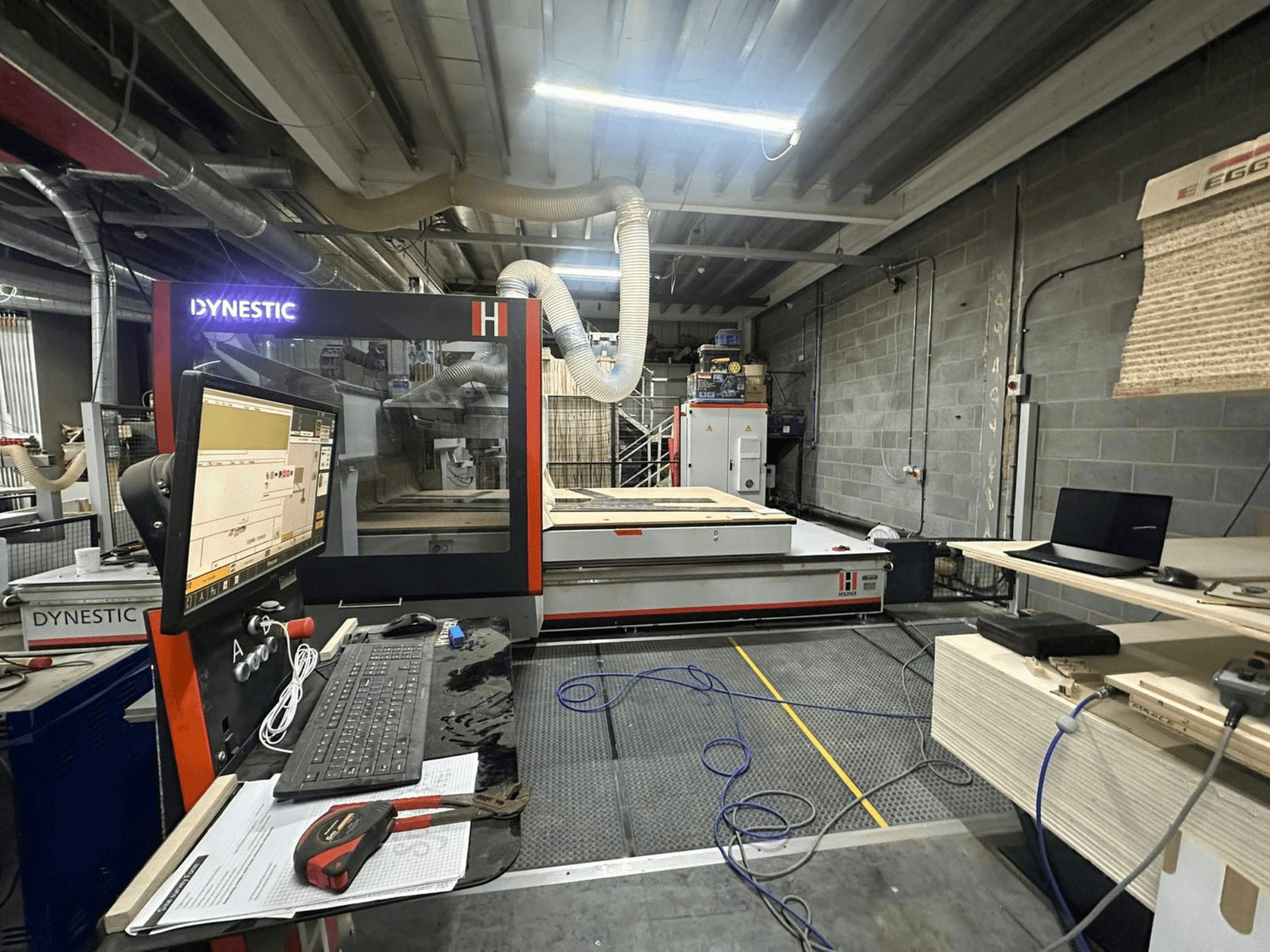 Molino de madera HOLZHER Dynestic 7535 en el taller, mostrando el panel de control, el monitor y los materiales en la mesa de trabajo, vista frontal.