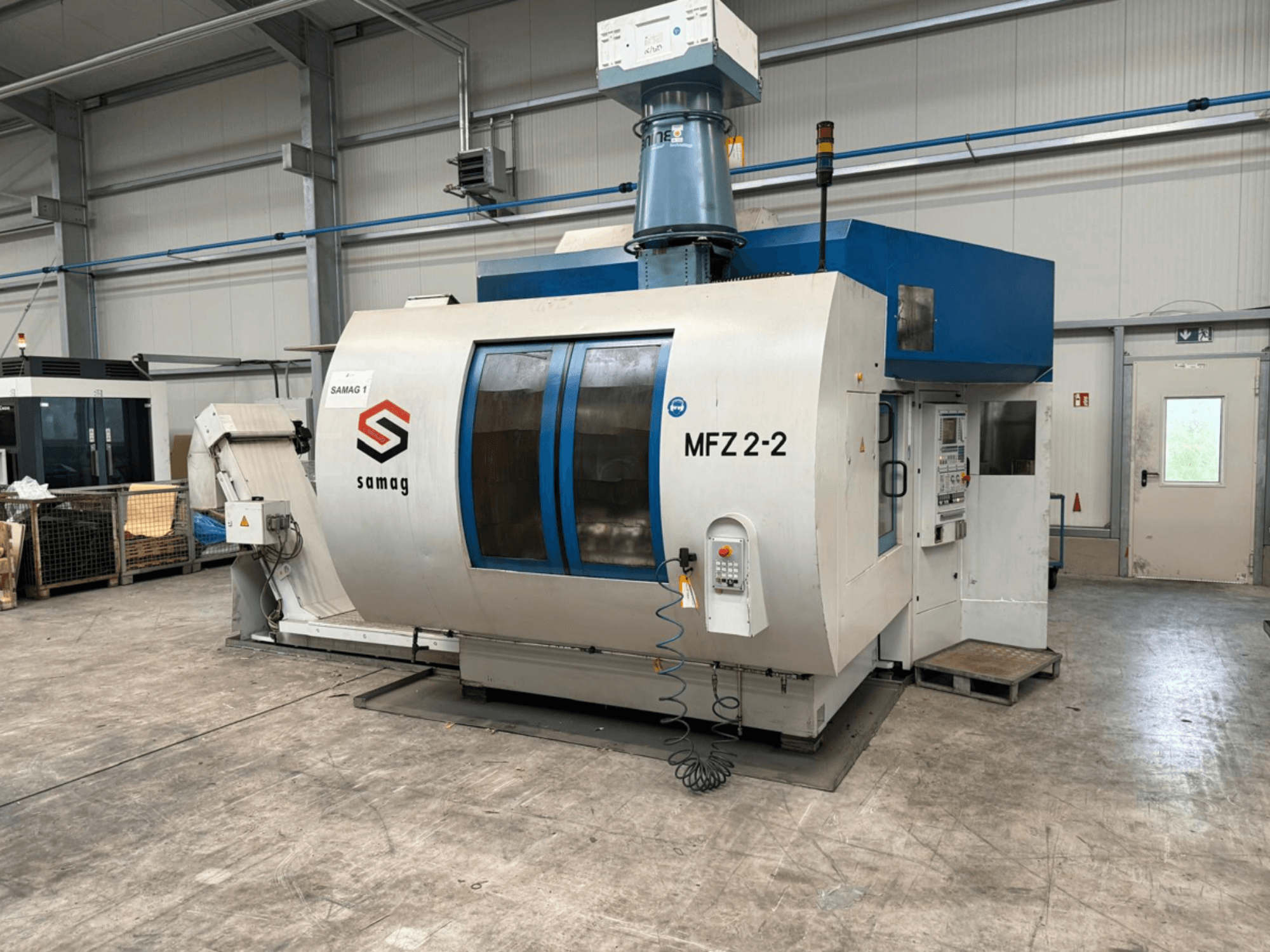 Máquina-herramienta Samag MFZ 2-2, vista frontal, mostrando el panel de control y la parte superior azul, con características de seguridad en un entorno industrial.