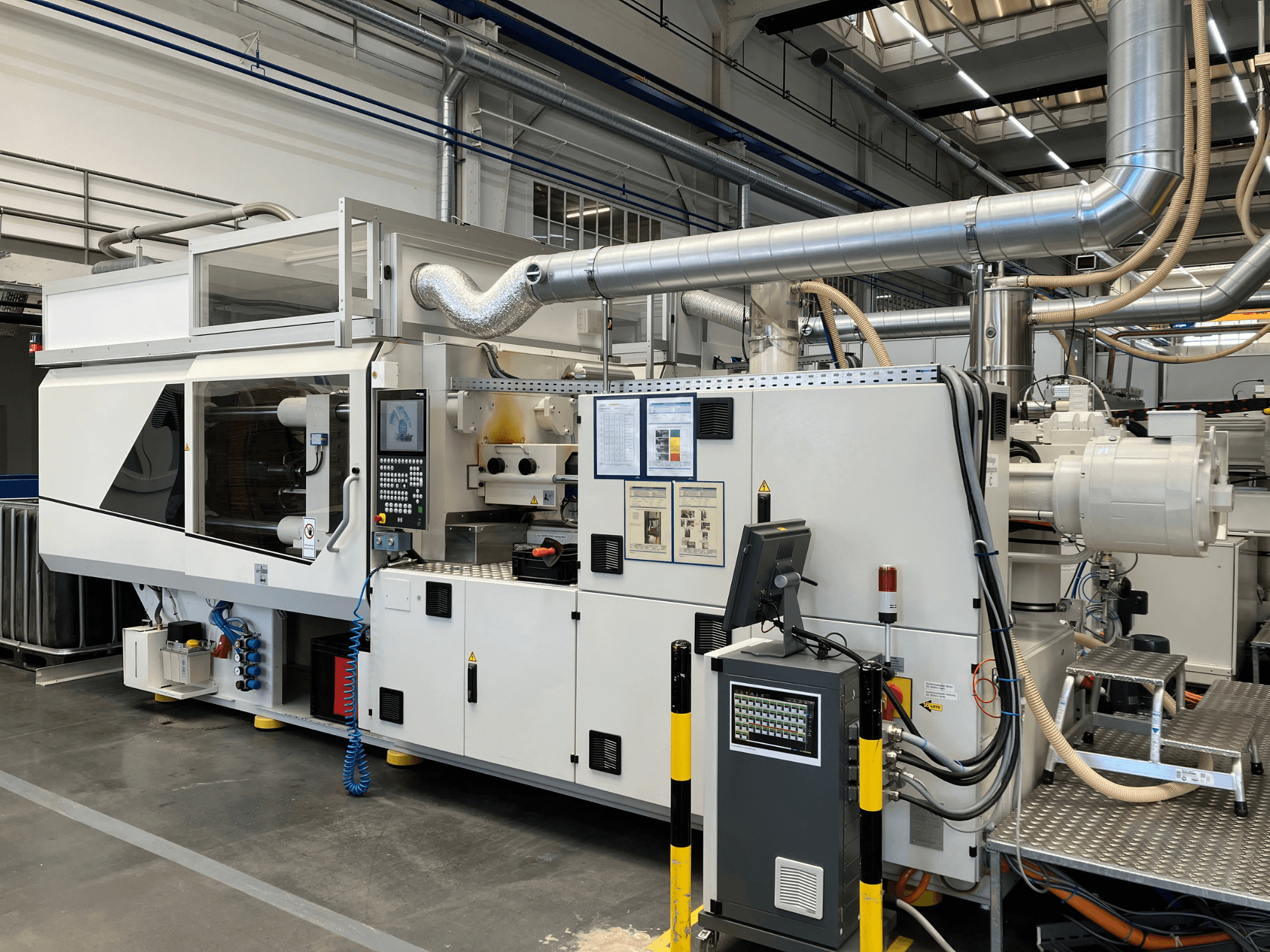 Vista frontal de una máquina industrial con panel de control, tuberías y pantallas de visualización, con un elegante diseño blanco y detalles técnicos.