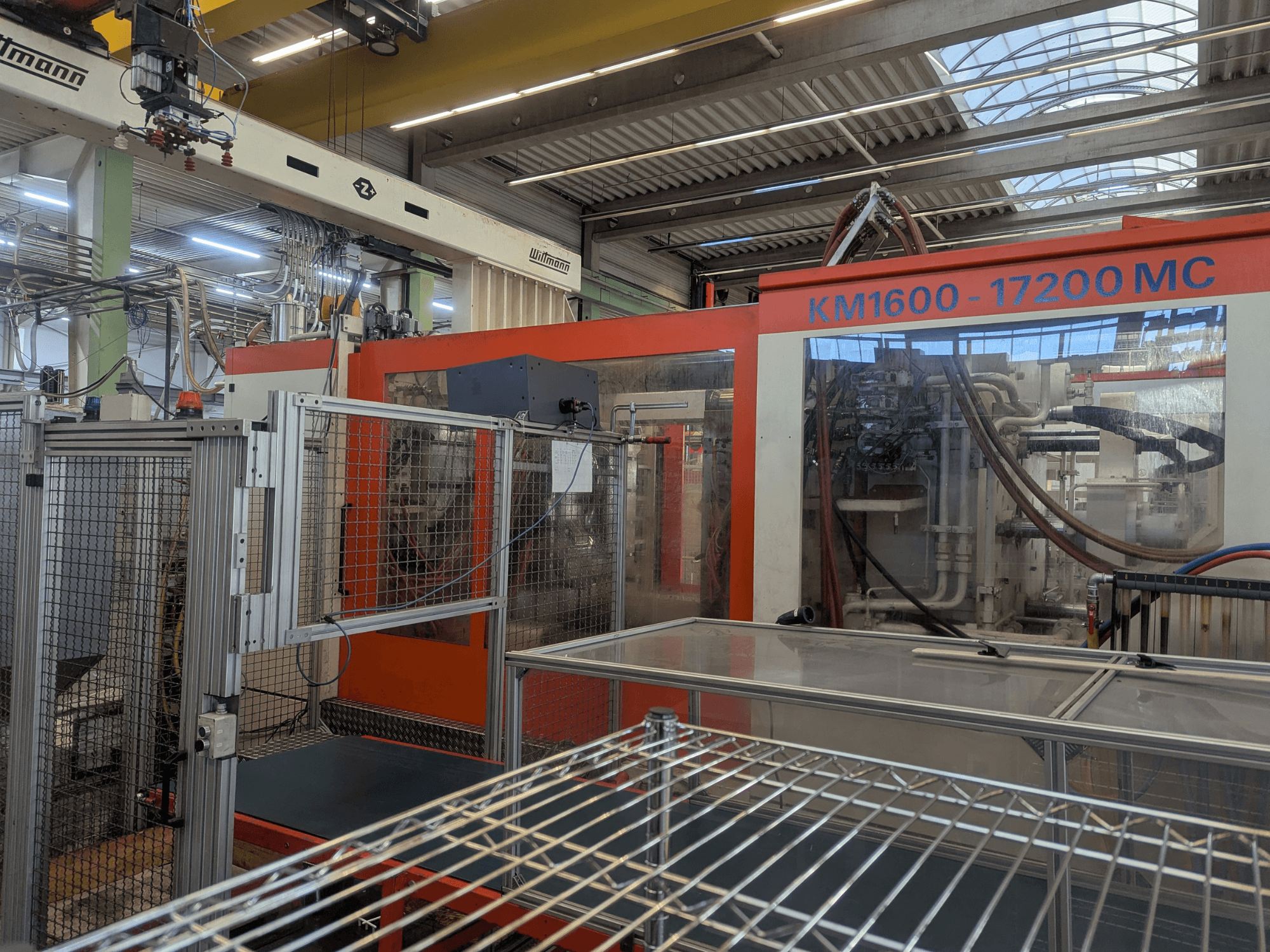 Máquina de moldeo por inyección hidráulica Krauss Maffei KM 1600-17200MC, vista frontal con panel de control visible y conductos hidráulicos.