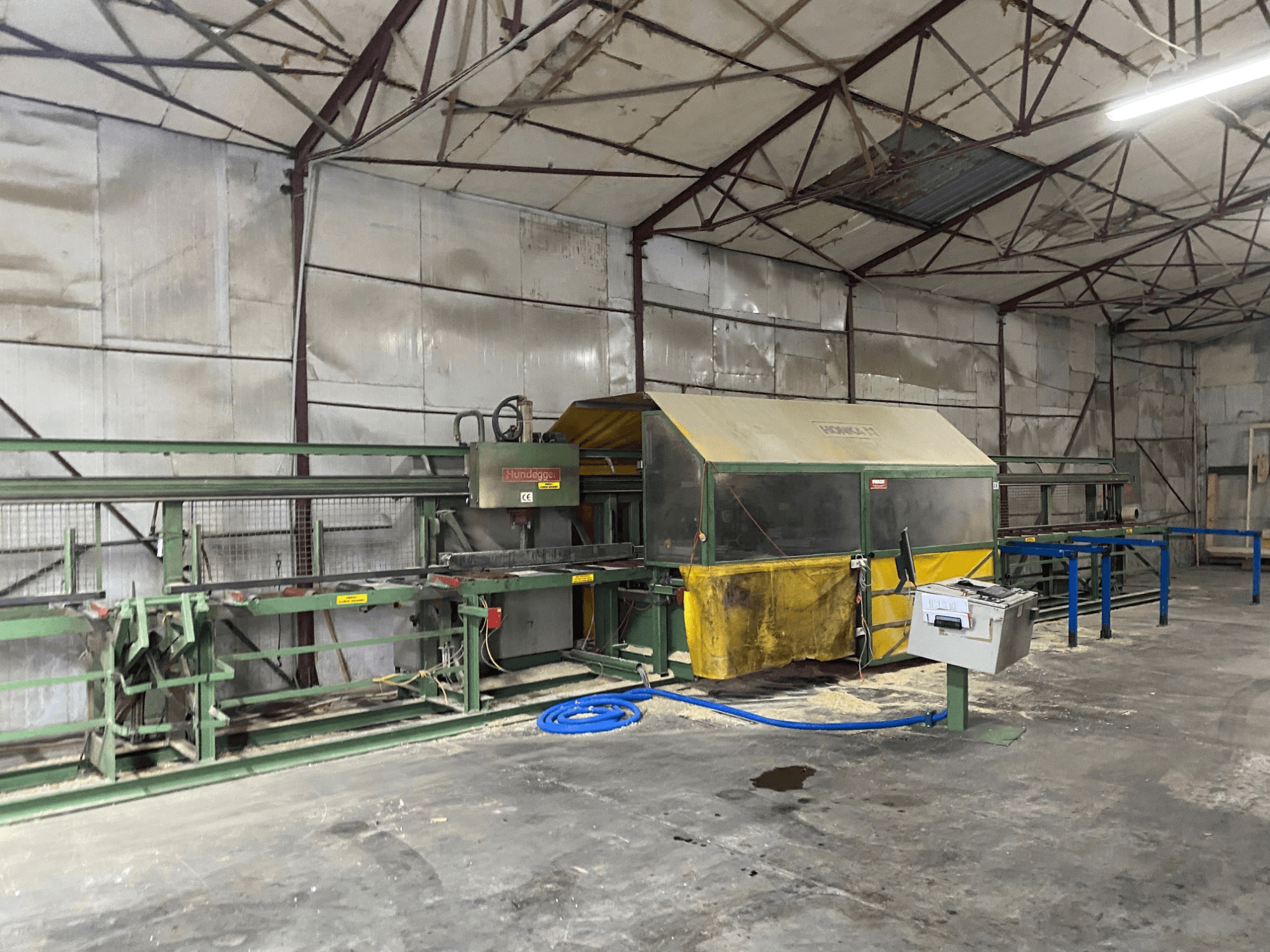 Centro de mecanizado de madera CNC HUNDEGGER K1 en un taller, vista lateral mostrando maquinaria, controles y serrín en el suelo.