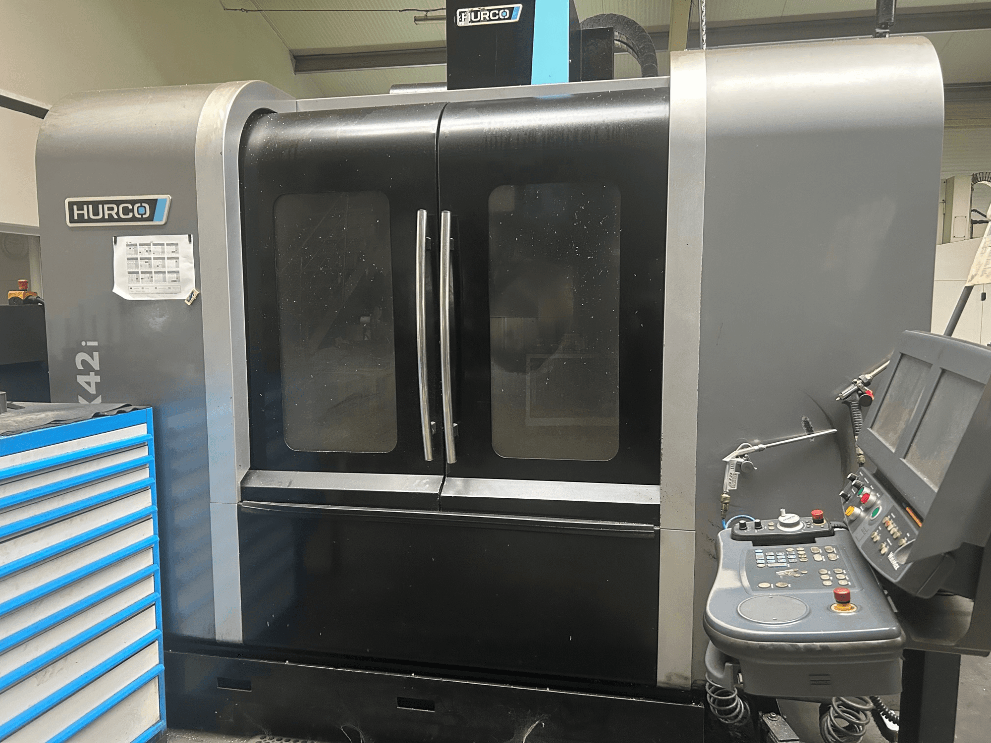 Máquina CNC Hurco VMX42i, vista frontal con panel de control en el lateral, presenta puertas dobles y detalles técnicos visibles.