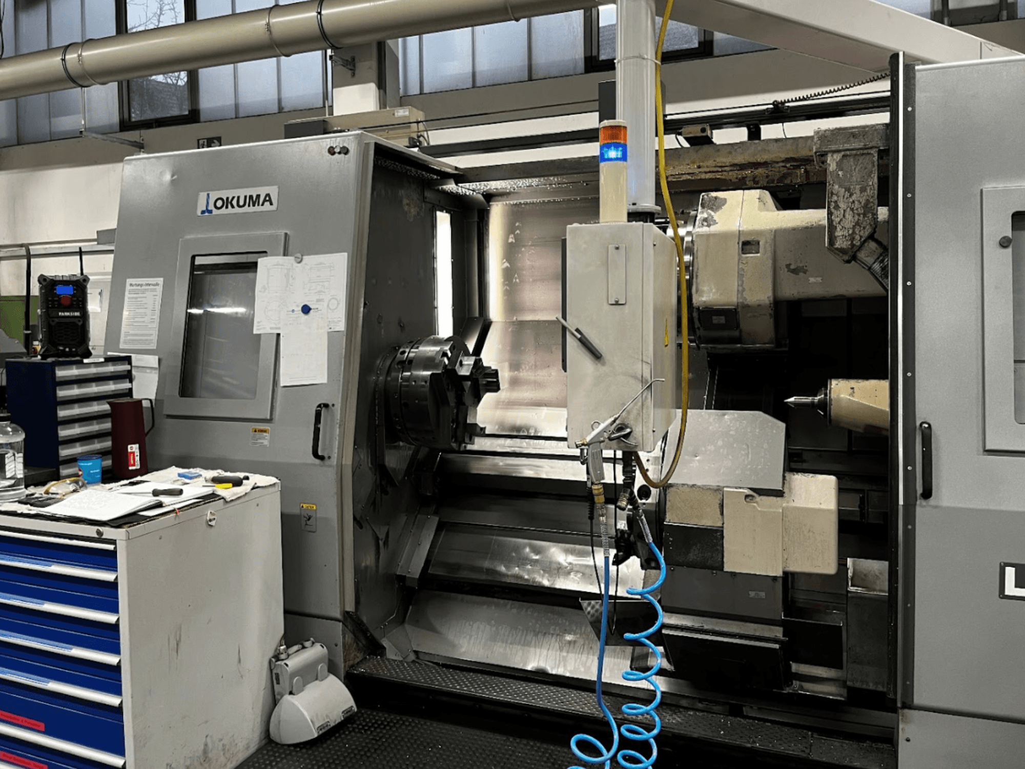 Torno horizontal Okuma LU35-M, vista frontal. Dispone de panel de control, herramientas y mandril grande para operaciones de mecanizado.